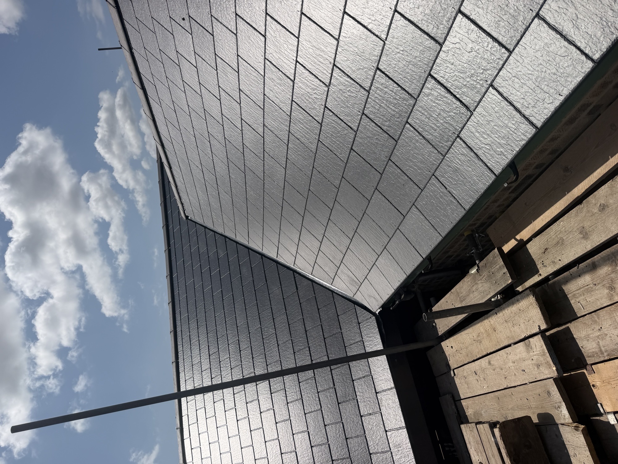 Completed dark slate roof planes meeting at a valley, viewed from scaffolding